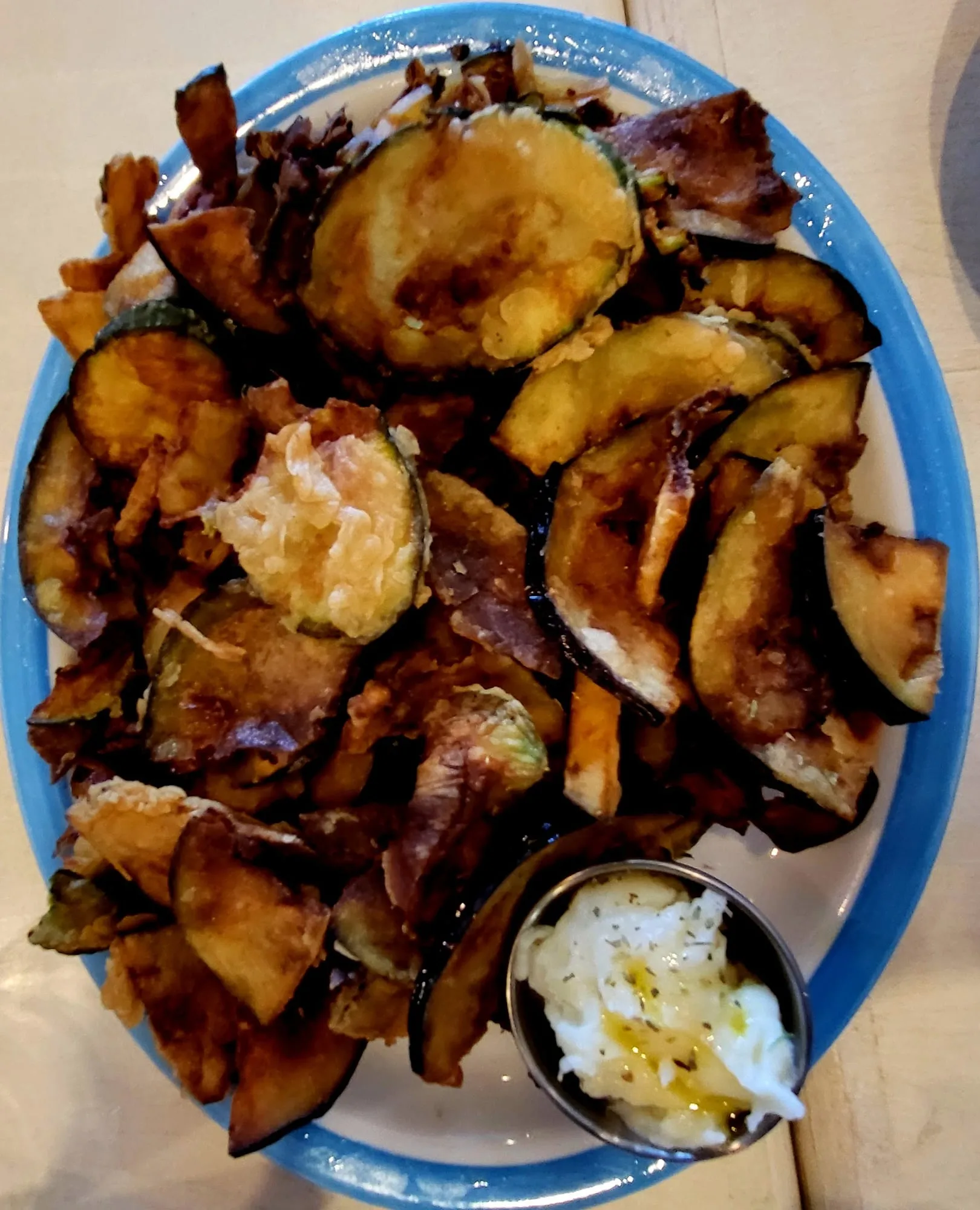 A blue-rimmed platter of fried eggplant and zucchini chips with a cup of skordalia