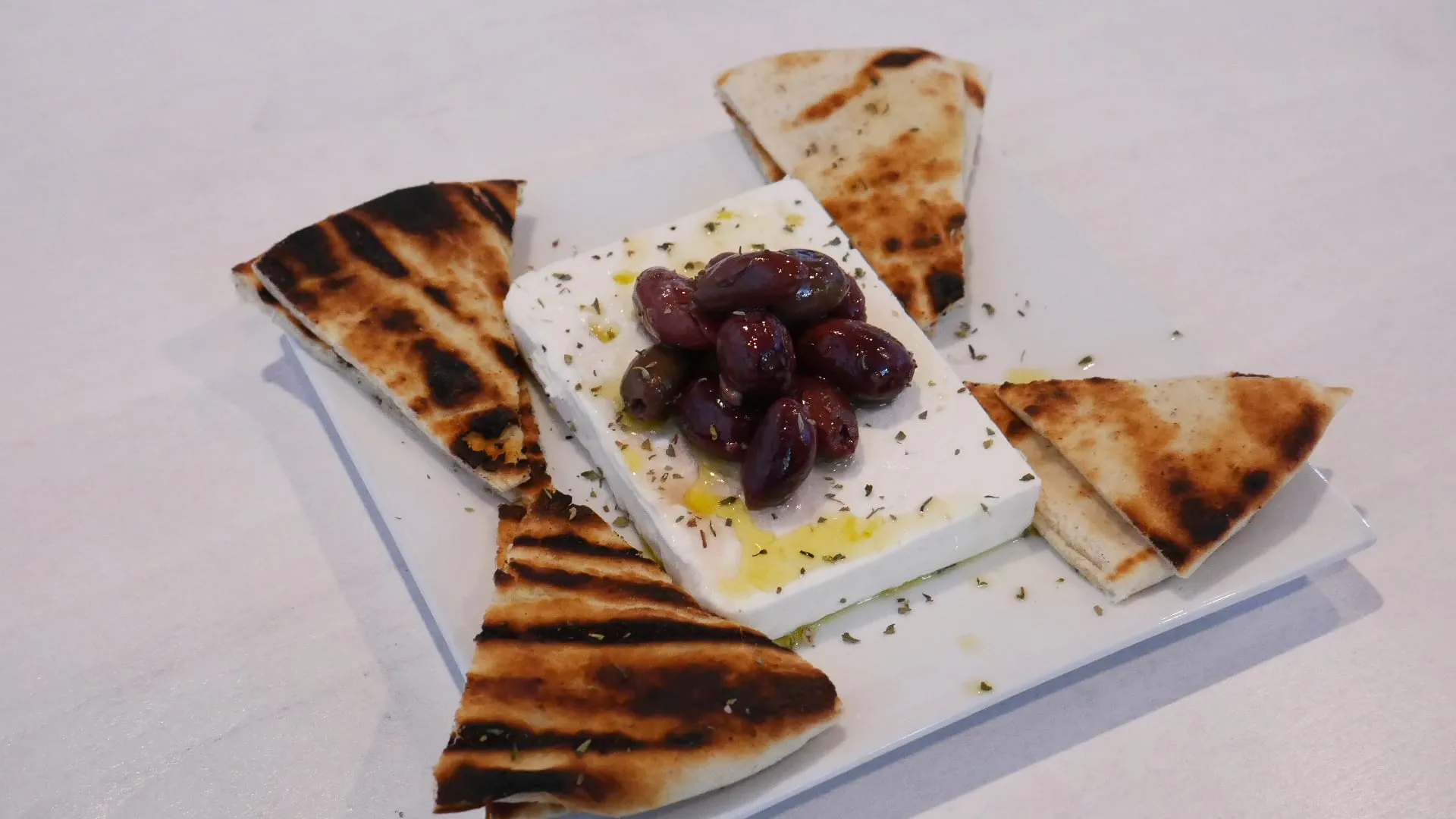 A block of feta with Kalamata olives and olive oil, with grilled pita