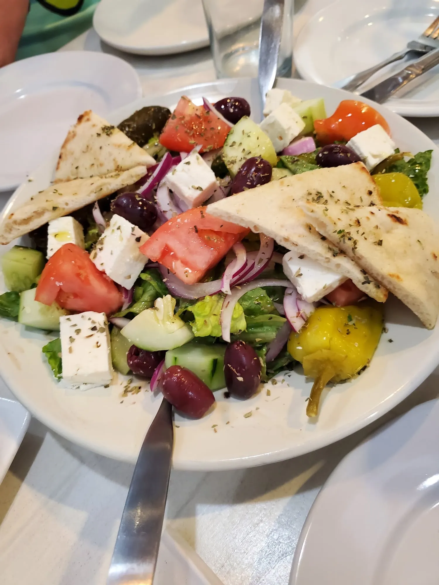 A Greek salad with tomato, cucumber, red onion, feta, Kalamata olives, a pepperoncini and pita