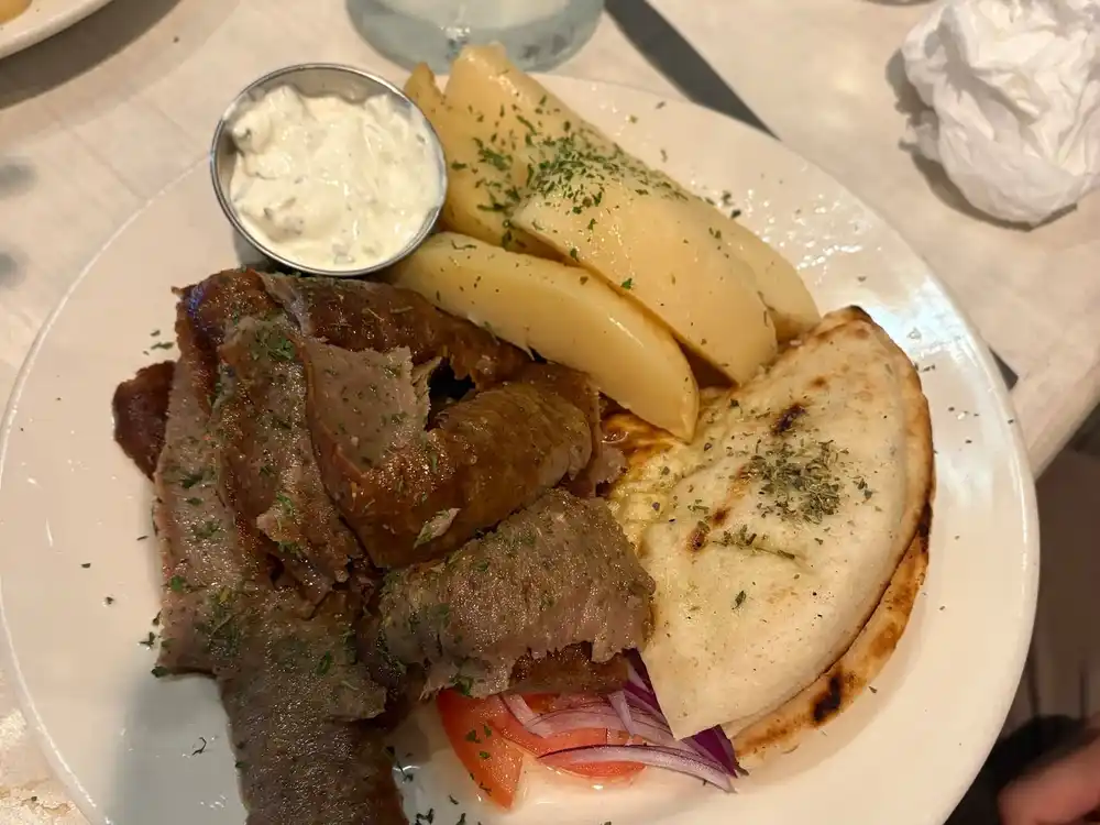 A gyro platter with sliced gyro meat, lemon potatoes, grilled pita, red onion and a cup of tzatziki