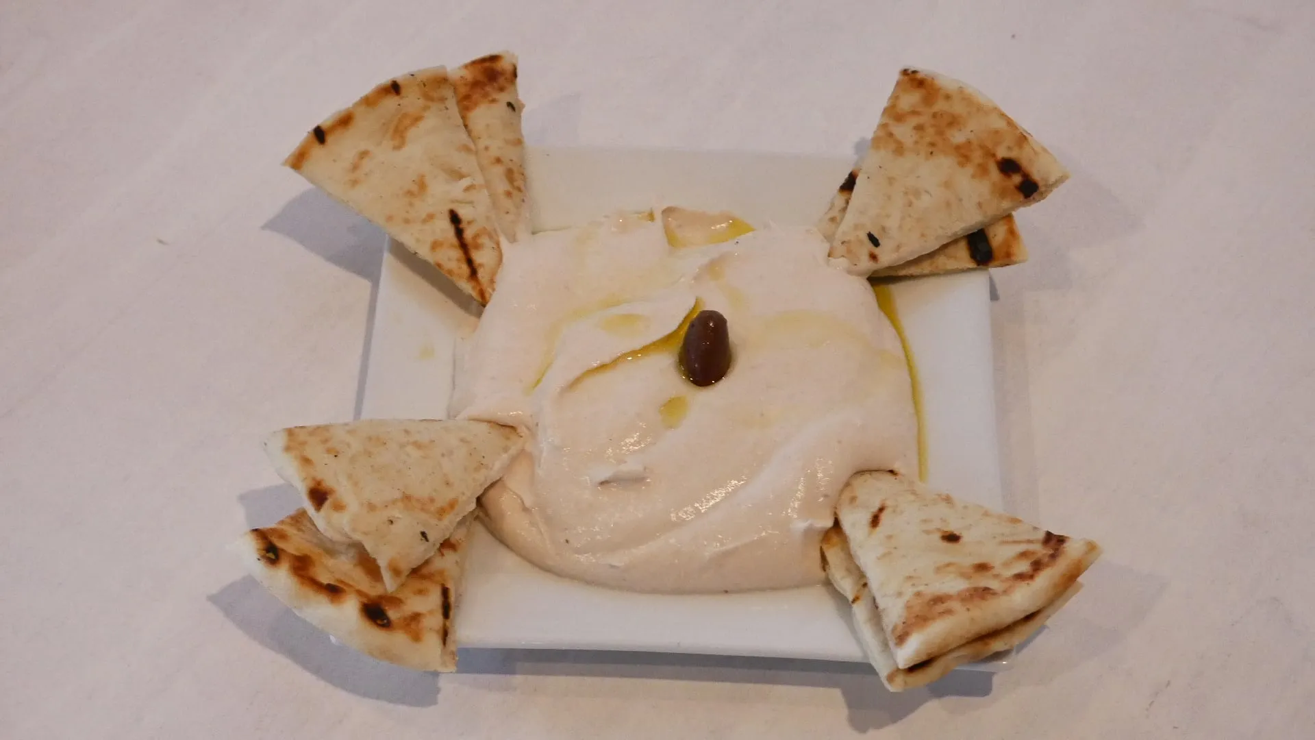 Hummus with olive oil and a Kalamata olive, with grilled pita