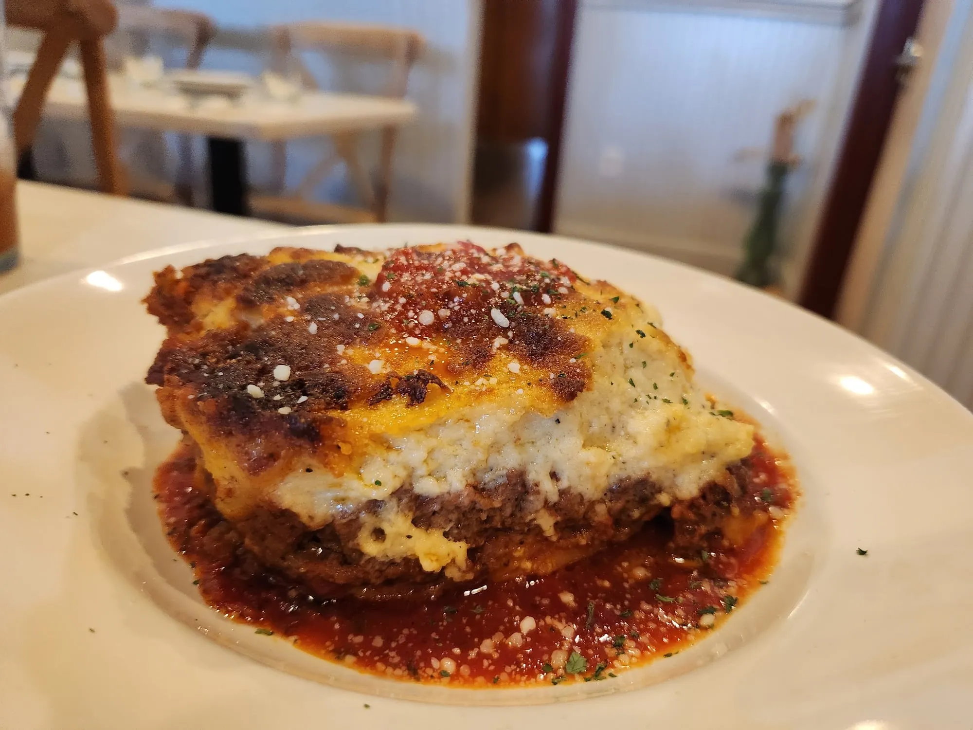 A slice of moussaka with browned bechamel over tomato sauce