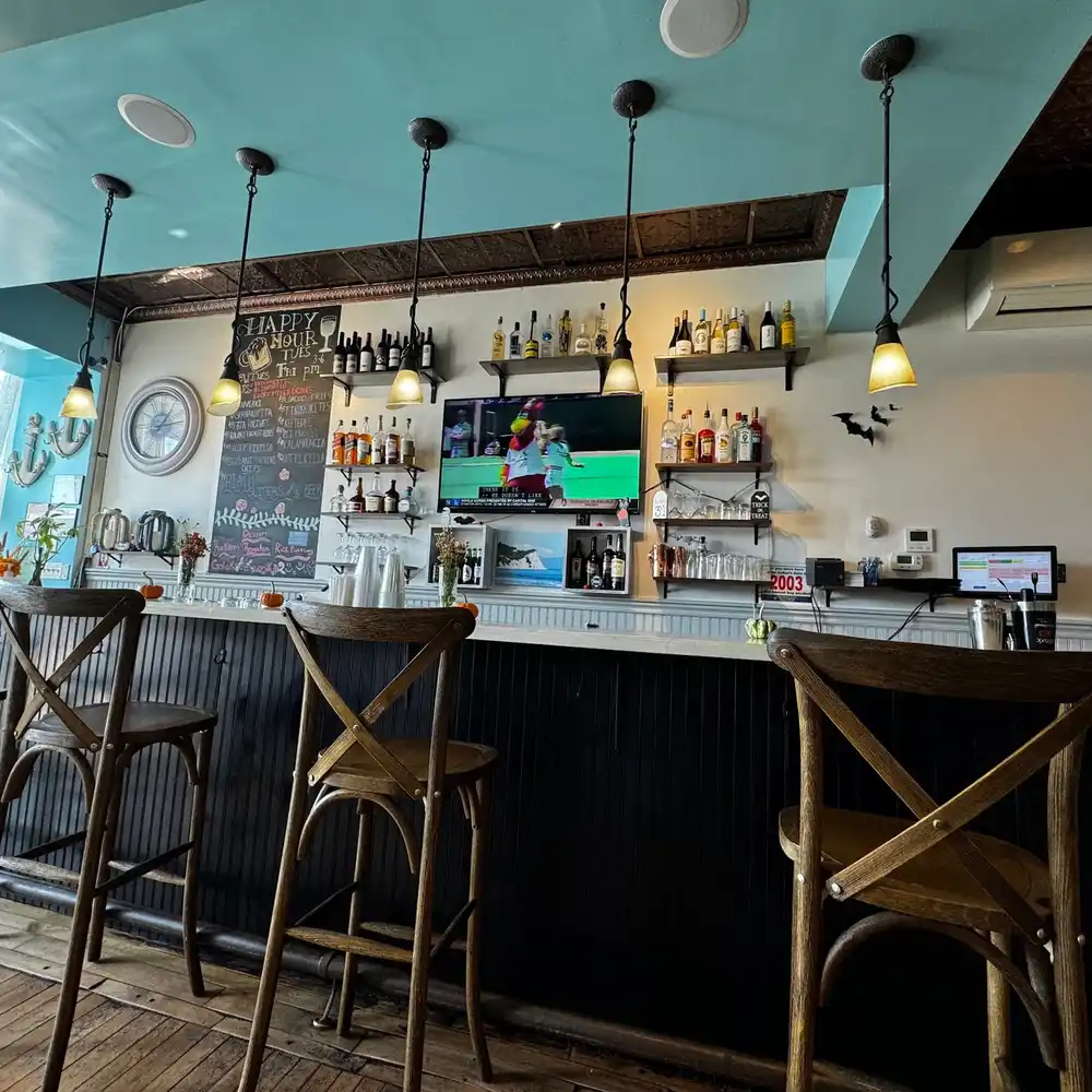 The bar, with crossback stools, shelves of bottles and a teal ceiling band