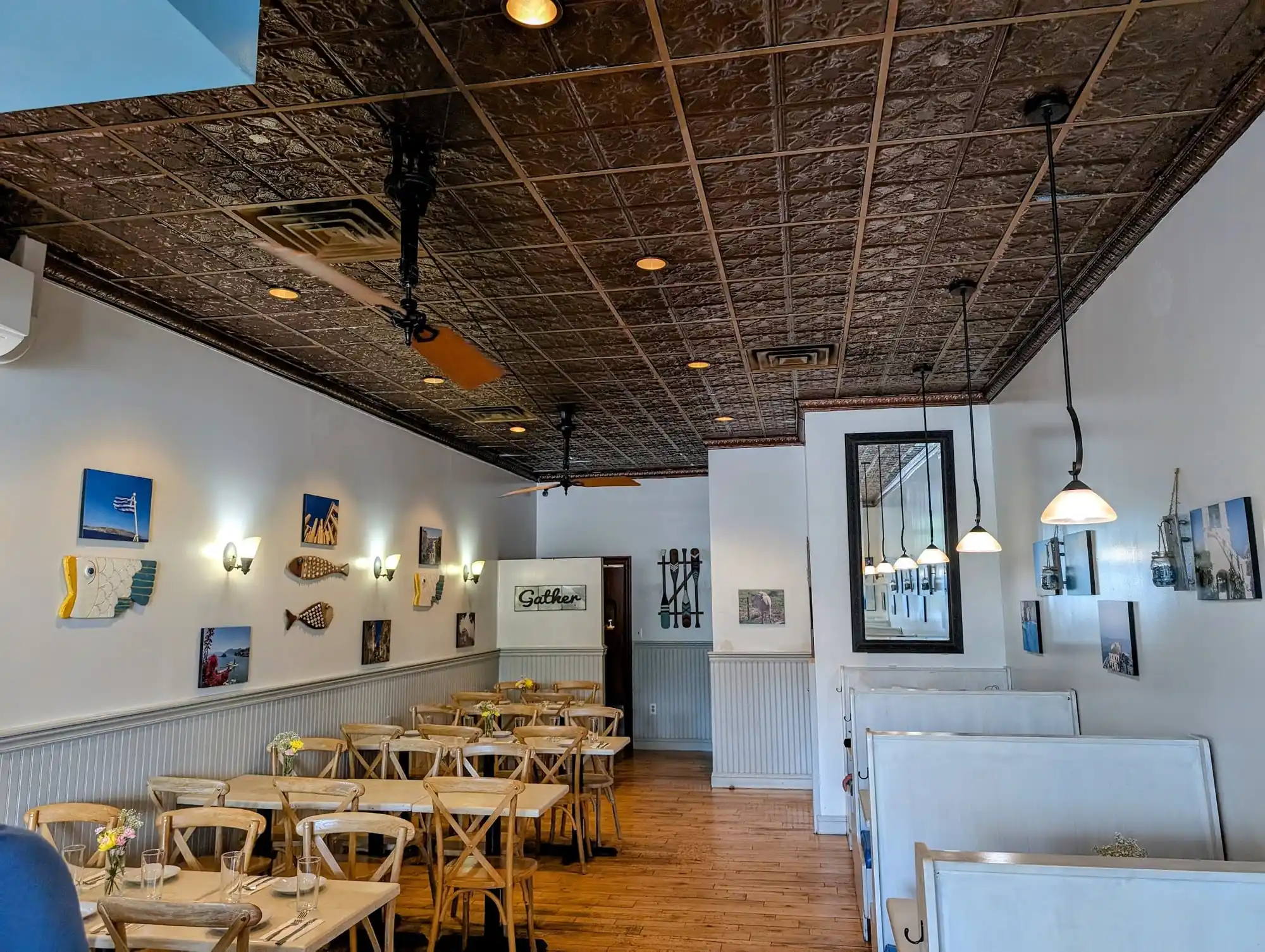 The dining room at Piato, with a pressed-tin ceiling, white beadboard walls hung with photos of Greek islands and wooden fish, and rows of set tables
