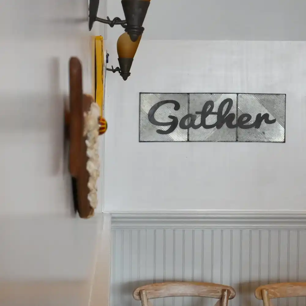 A "Gather" sign and a wall sconce above the white beadboard in the dining room