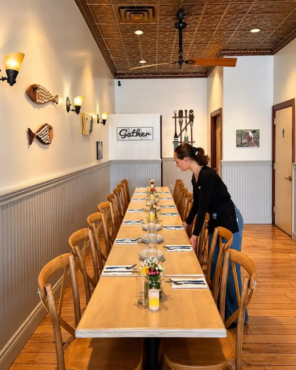 A long table set for a party in the dining room, with flowers, glasses and crossback chairs